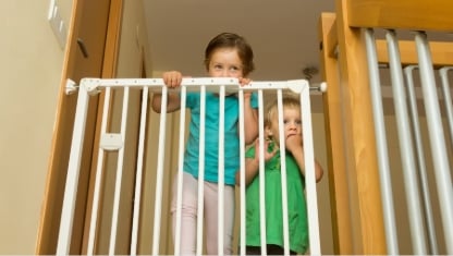 Two little girls approaching safety gate of  stairs at home