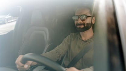 Confident businessman driving a car on a sunny day. Looking relaxed and happy. Wearing sunglasses.