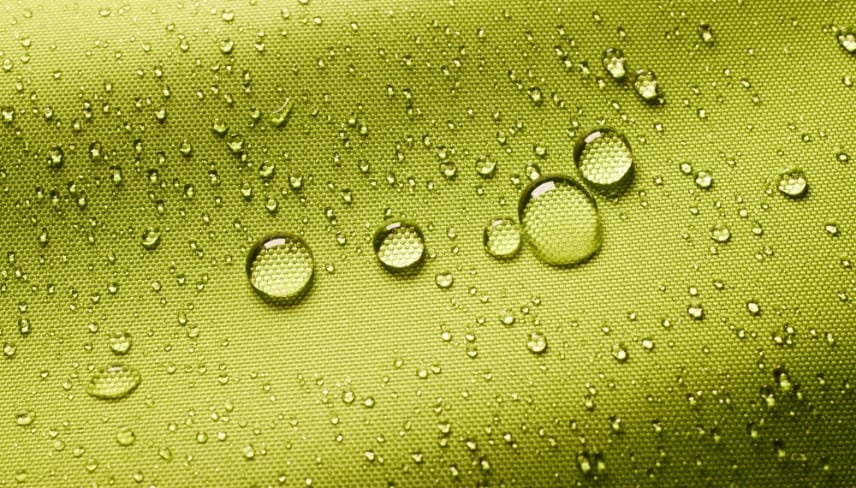 Top view closeup of green background with small round drops of water on textured waterproof impregnated fabric in light room