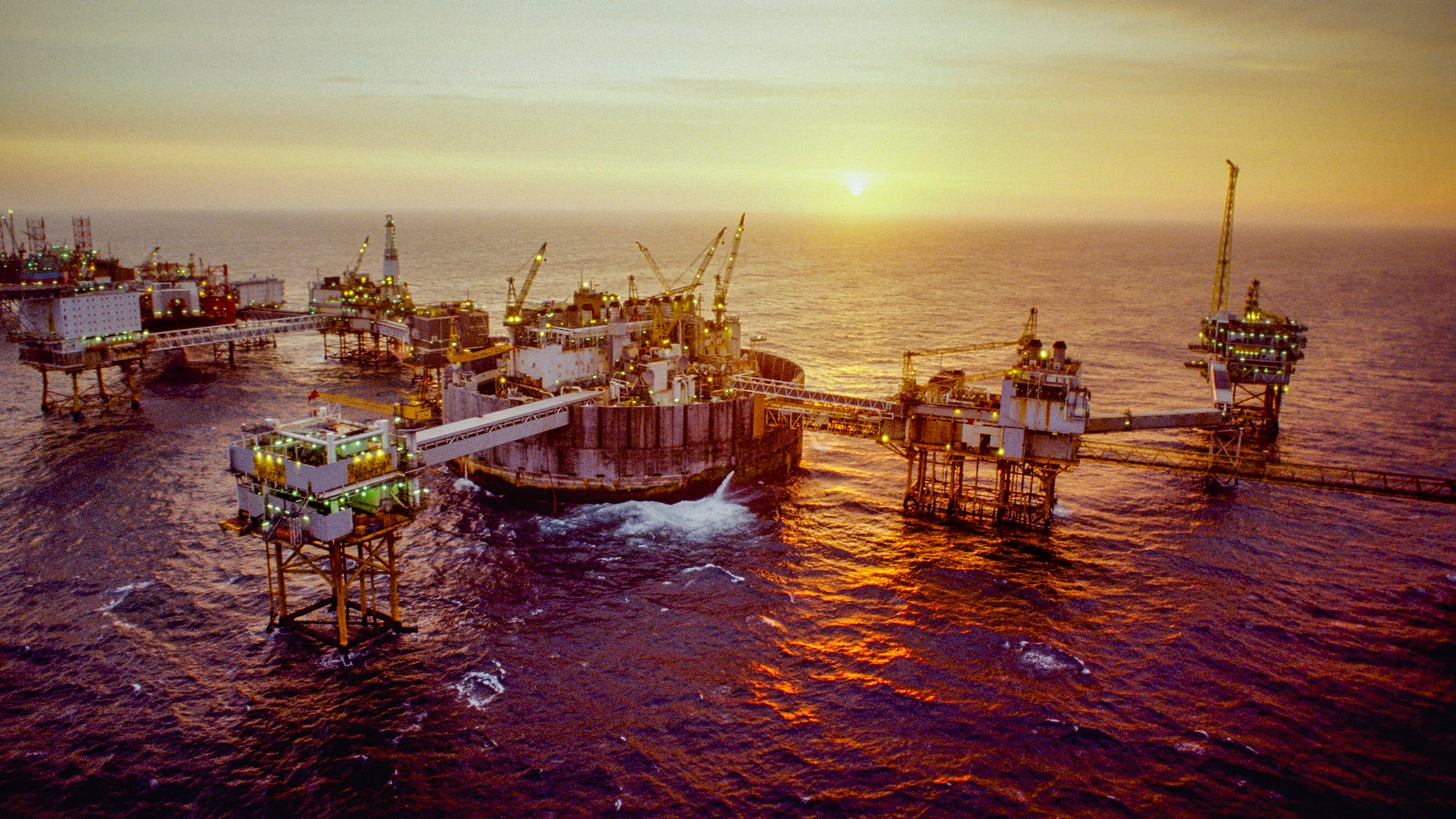 large connected oil rigs in offshore waters with yellow sunrise in the background 